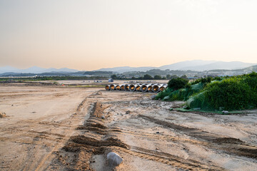 Expansive construction site with exposed earth and heavy machinery tracks. Surrounded by distant...