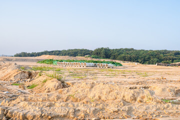 Expansive construction site with exposed earth and heavy machinery tracks. Surrounded by distant...
