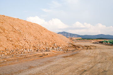Expansive construction site with exposed earth and heavy machinery tracks. Surrounded by distant mountains, the scene captures early stages of land development and earthmoving operations.