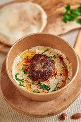 Delicious Homemade Hummus with Spiced Meatball Garnish Surrounded by Fresh Herbs and Olive Oil in Natural Bowl