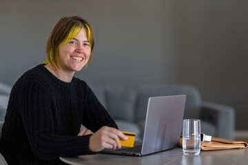 upper body of woman in black sitting at table with laptop computer and credit card