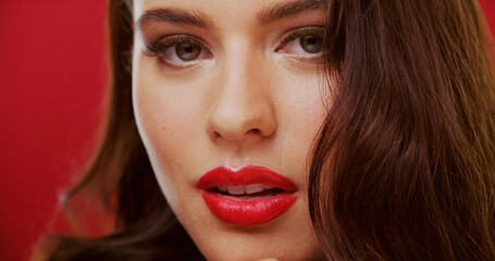 Fototapeta premium Portrait, lipstick and woman in studio for beauty, makeup and cosmetology with face on red background. Lips, female person with glamour or bold color for luxury cosmetics with aesthetic and glow