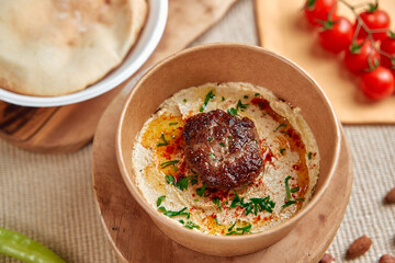 Delicious Hummus Bowl with Flavorful Meatball and Fresh Ingredients Served on a Wooden Board for a...
