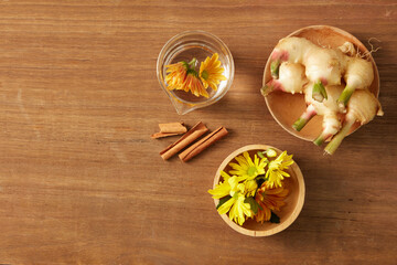 Flat lay with ginger, calendula, cinnamon, and a glass of floral infusion on a wood background. A soft herbal setup perfect for displaying natural beauty or essential oil products.