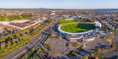 Aerial panorama of a city arterial road separating a factory and a football oval and carpark
