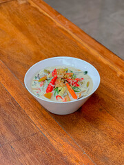Traditional Indonesian garang asam vegetable soup served in a white bowl on rustic wooden table. Rich coconut broth, vibrant colors, perfect for culinary stock imagery