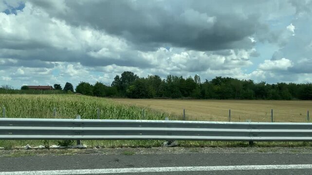 Scenic view of rural cultivated fields and a dense tree line alongside a highway guardrail in Bologna, Italy. 4K