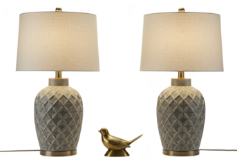 A pair of decorative table lamps with textured bases and a small bronze bird figurine in between, isolated on transparent background