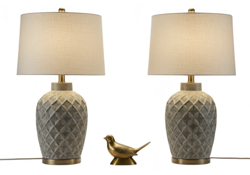 A pair of decorative table lamps with textured bases and a small bronze bird figurine in between, isolated on transparent background
