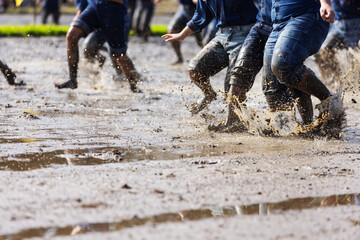 A group of people walks barefoot through wet, muddy soil, increasing exposure risk to soil-borne diseases. 