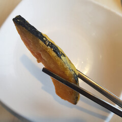 A close-up of a hand holding a piece of fried pumpkin, a crispy and savory Korean snack.