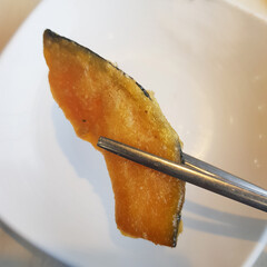 A close-up of a hand holding a piece of fried pumpkin, a crispy and savory Korean snack.