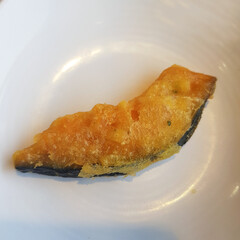 A close-up of a hand holding a piece of fried pumpkin, a crispy and savory Korean snack.