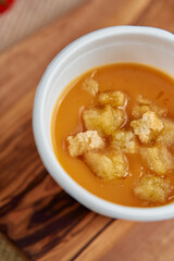 Delicious Bowl of Warm Orange Soup Topped with Crunchy Croutons Served in a White Cup on a Wooden...