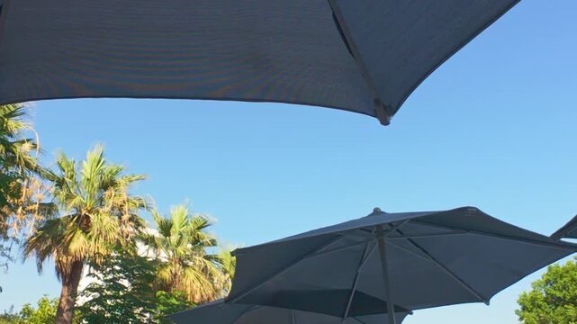 Sunbath concept. Under the umbrella by the pool at the hotel. Blue sky and beach umbrella 4k video. Summer vacation, resort hotel. 	