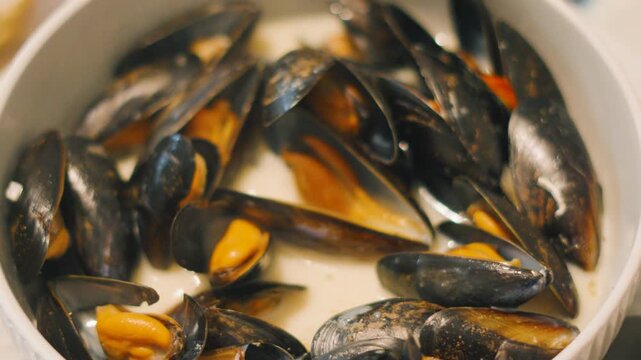 Top Overview of Mussels as Hand Reaches In and Takes Shellfish Out to Eat. Mollusks in White Wine Sauce.