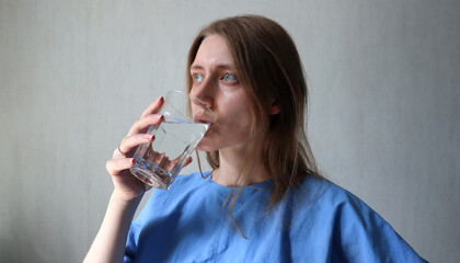 Woman drinking water. Caucasian, blond hair loose. Blue eyes and shirt. Holding clear glass of...