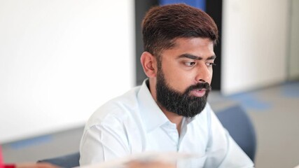 Professional Indian businessman in light blue shirt attentively listens during an office meeting. Focused specialist appears serious and engaged in business discussion. Diligent male model working. - Powered by Adobe
