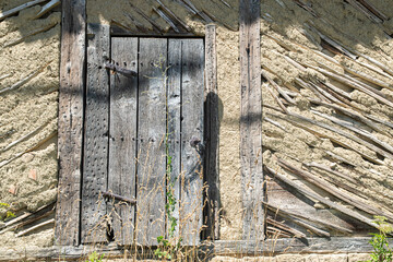 An old, rustic wooden door in a textured clay and timber barn wall closeup as rural background