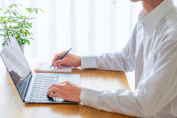 ノートパソコンで作業しメモを取るビジネスパーソン