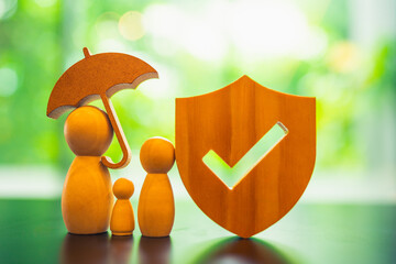 A wooden sculpture of a family stands together under an umbrella with an insurance symbol. This...