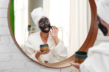Enjoying self-care with a charcoal face mask in a bright, modern bathroom while admiring...