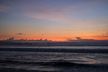 Golden sunset paints the sky over Kuta Beach, Bali, blending warm orange and purple hues above calm ocean waves, creating a serene and breathtaking view along the horizon of this tropical coast.