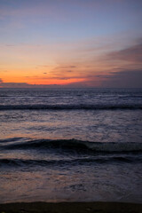 Golden sunset paints the sky over Kuta Beach, Bali, blending warm orange and purple hues above calm ocean waves, creating a serene and breathtaking view along the horizon of this tropical coast.
