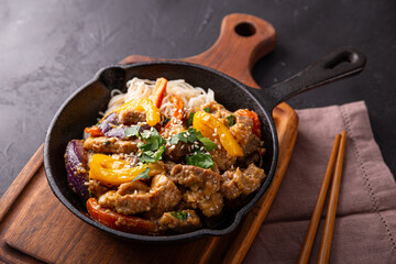 Asian pork with vegetables and glass noodles in a pan on the black background