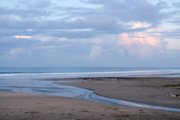 Peaceful morning atmosphere at Seminyak Beach, Bali, where soft waves meet wide stretches of sand under pastel skies, creating a serene coastal view with gentle colors and quiet reflections.