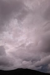  dark rain clouds float across the blue sky, evening, sunset, lightning illuminates the storm clouds, a landscape with clouds and mountains, and trees
