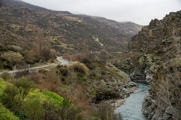 A curving road passes through rugged hills and alongside a rocky gorge with a flowing river in New...