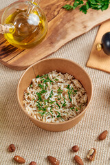 Deliciously Cooked Rice with Fresh Herbs Served in a Paper Bowl Accompanied by Olive Oil and Almonds on a Rustic Table Setting