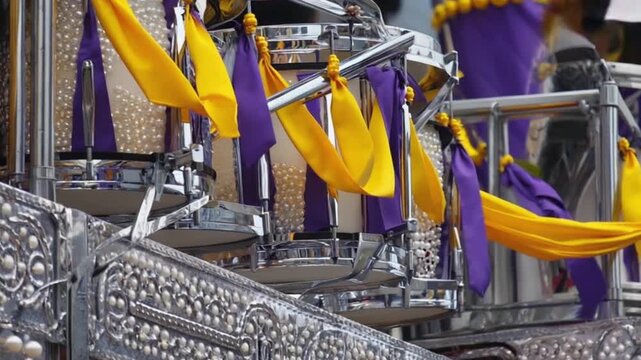 Colorful parade float featuring shiny drums adorned with vibrant purple and gold ribbons