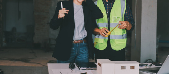 Construction manager and engineer dressed in orange work vests and hard helmets explore...