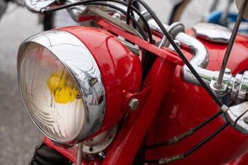A Red motorcycle with a yellow headlight. The headlight is dirty and has a yellow light