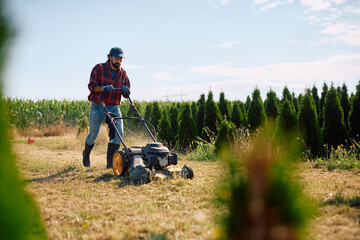 Male worker mowing lawn at plant nursery.