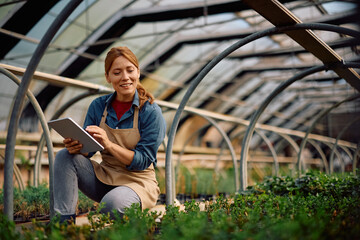 Happy female botanist using touchpad while working at plant nursery.
