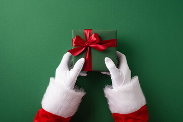 A close-up of Santa Claus giving a beautifully wrapped Christmas gift with red ribbon. Symbolizes...