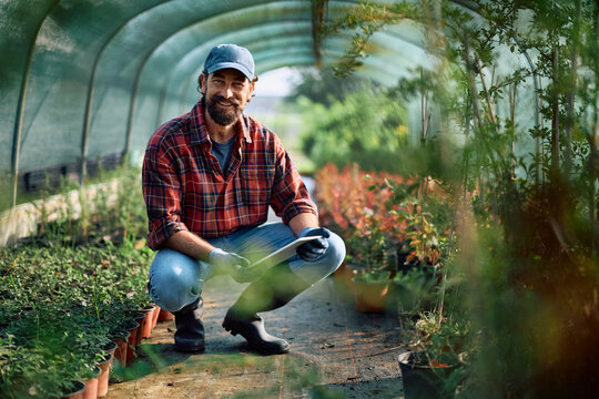 Happy greenhouse owner using digital tablet and looking at camera. - Powered by Adobe