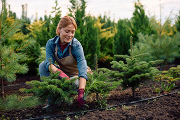 Happy female gardener working at plant nursery.