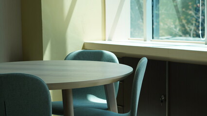 Minimalist modern office interior with a round wooden table and upholstered chairs near a large sunlit window, perfect for business, workspace, or lifestyle concepts.