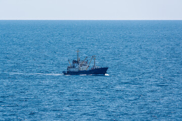 Fishing boat in blue sea and clear sky with birds flying overhead.