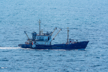 Fishing boat in blue sea and clear sky with birds flying overhead.