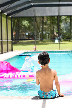 Shirtless boy sits poolside looking at colorful float toys