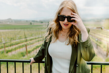 Woman adjusts sunglasses while standing at scenic vineyard