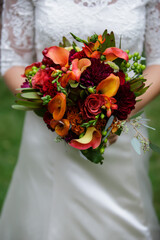 Bride holding vibrant autumn bouquet of reds and oranges.