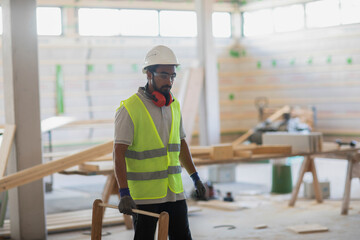 worker with helmet and safety jacket working in a wooden hall