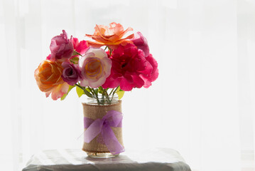 Colorful roses blooming in rustic vase by sunlight window