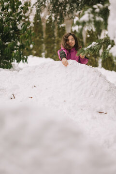 Child in pink jacket playing atop large snowy mound outdoors